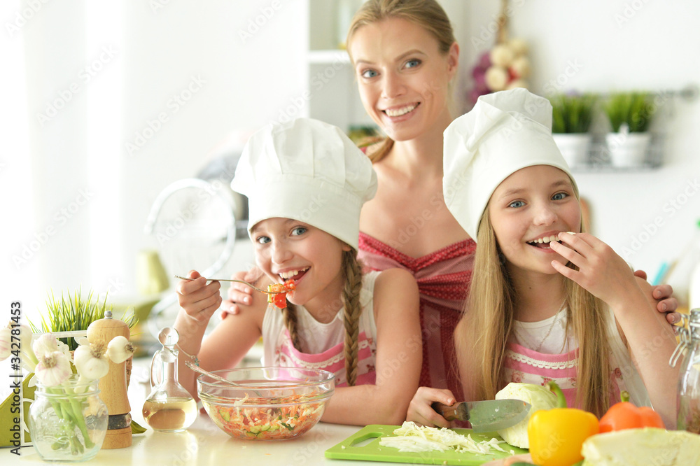 Cute girls with mother preparing delicious fresh salad in kitchen Cute girls with mother preparing delicious fresh salad in kitchen