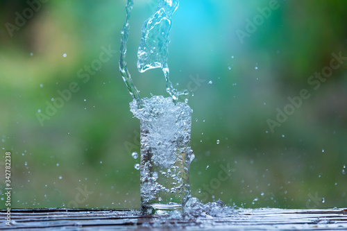 Drink water pouring in to glass over sunlight and natural green background.Water splash in glass Select focus blurred background