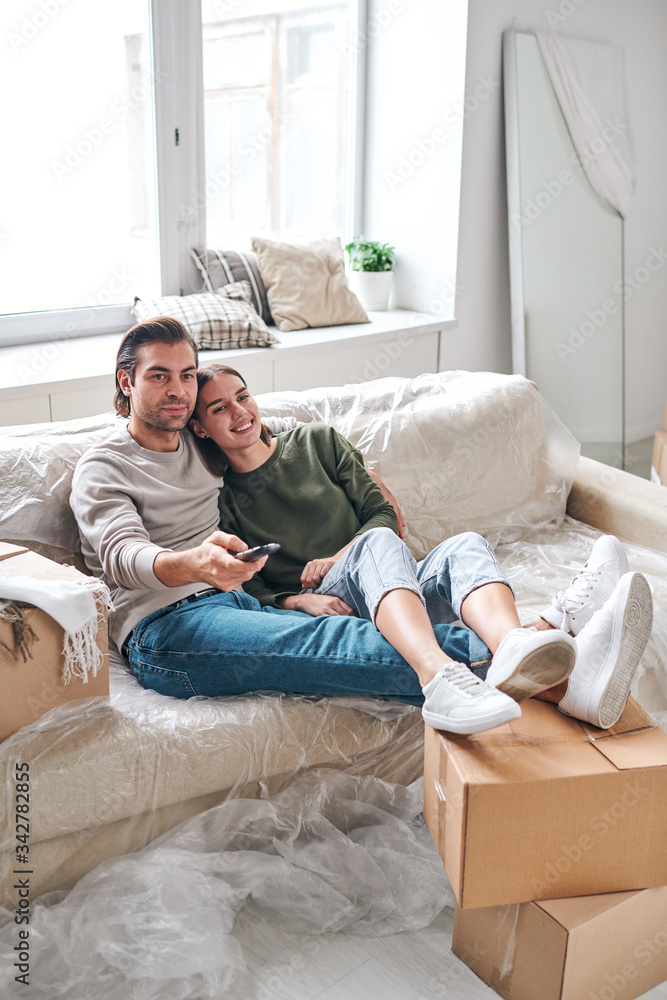 Happy young restful couple relaxing on couch while sitting in front of tv set