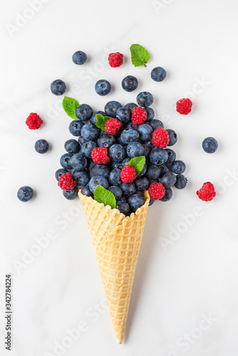 wildberries blueberry and raspberry with mint in waffle ice cream cone on white marble background. top view. flat lay photo