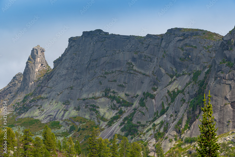 rocky ridge under blue sky in mountain valley, journey of climbers on sheer cliffs