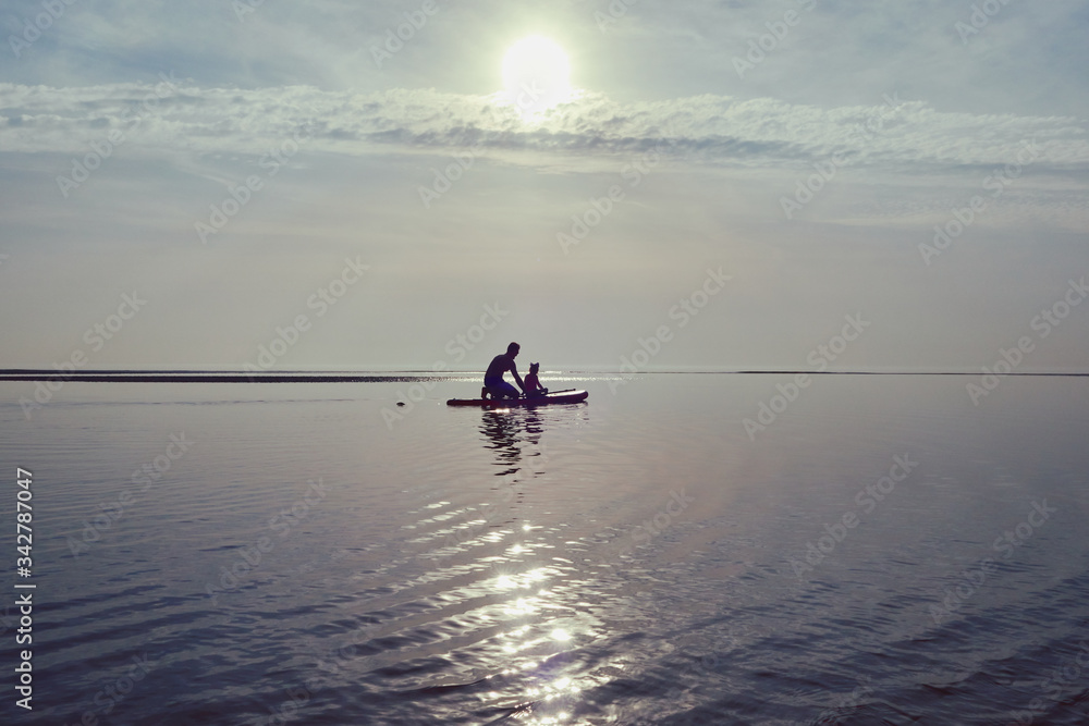 A silhouette of a father and daughter on a paddle board on a beautiful summers day on the calm ocean. Relaxing family bonding time with water sports and exercise. soft and hazy days.