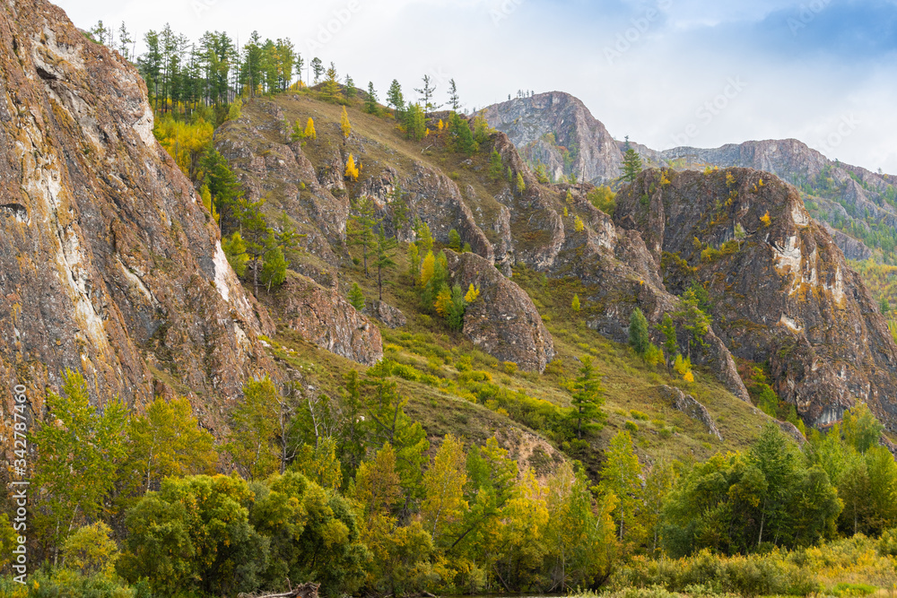 Rock mass along river, mountain cliff with autumn forest