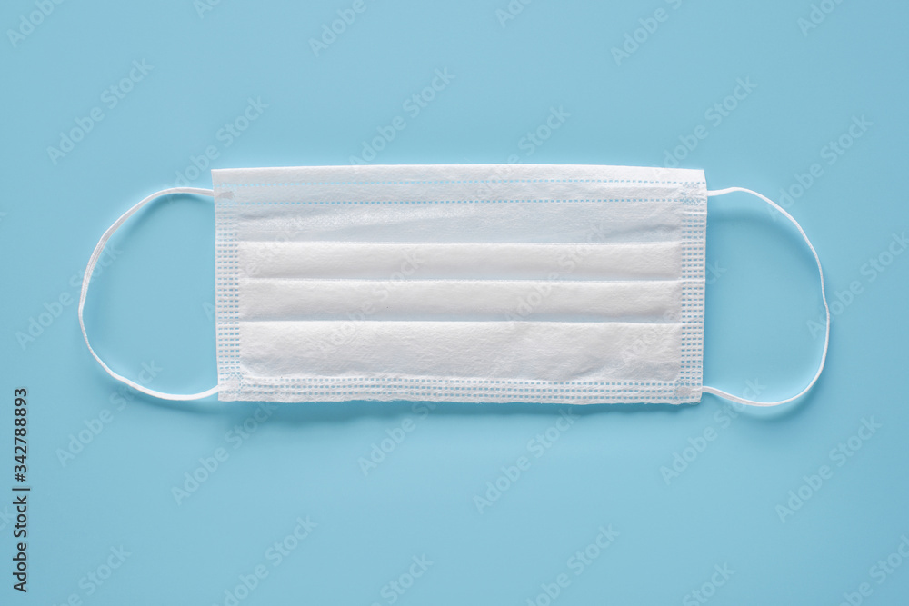 Obraz premium Medical mask on blue background. Typical 3-ply surgical mask to cover the mouth and nose. Procedure mask from bacteria. Healthcare and protection concept.