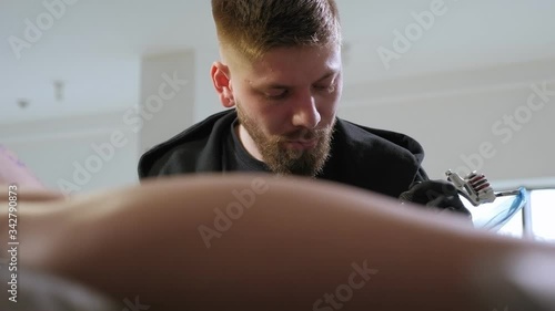 Portrait of a modern tattoo artist while working with a client. A professional tattoo artist makes a tattoo on the leg of a young girl in a tattoo parlor. photo