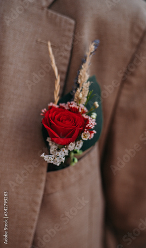 a small bouquet of red roses and dried flowers inserted into the pocket of a brown men's jacket