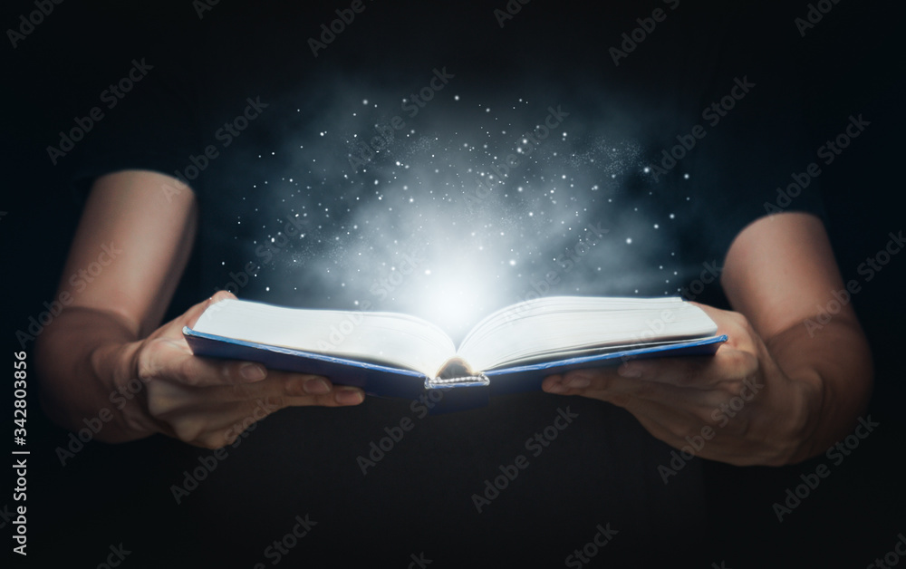 Man open magic book with growing lights and magic powder floating on the book, Learning, Education, Knowledge and religion concept.