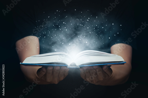 Man open magic book with growing lights and magic powder floating on the book, Learning, Education, Knowledge and religion concept. photo