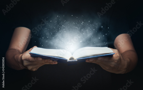 Man open magic book with growing lights and magic powder floating on the book, Learning, Education, Knowledge and religion concept. photo