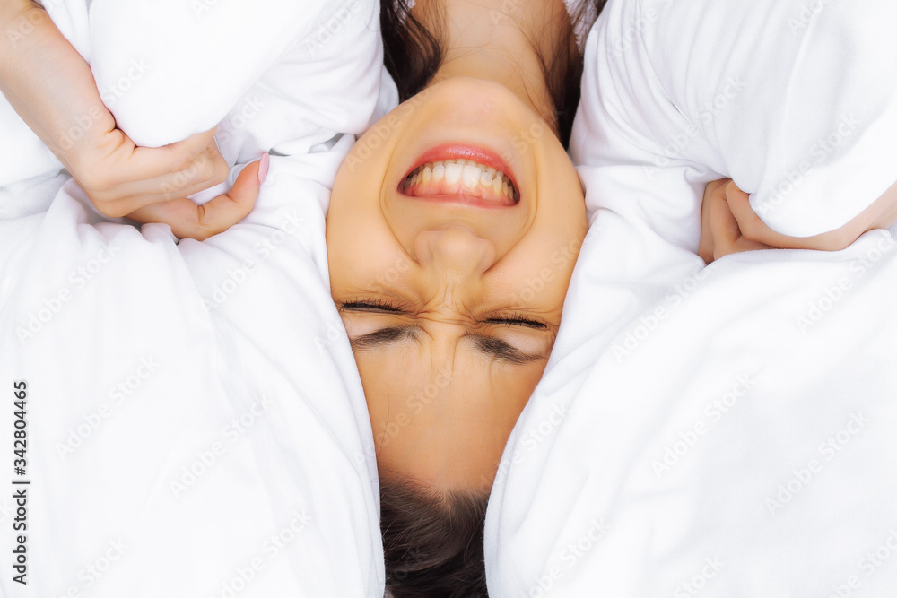 Severe headaches. Annoyed woman shouts while lying in bed. The girl closes her ears with a pillow. Severe headaches. Annoyed woman shouts while lying in bed. The girl closes her ears with a pillow.