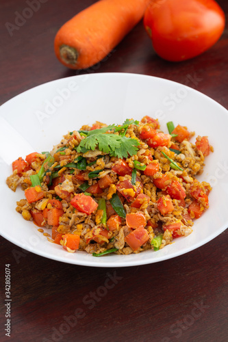 Homemade Scrambled eggs with carrots and tomatoes in white plate on wooden table.