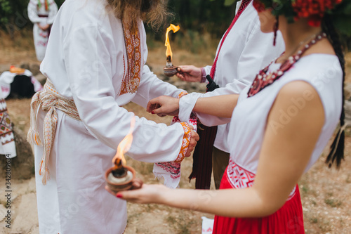 A bearded ataman knotted a knot with a rushnyk to the newlyweds at the wedding ceremony of Ukrainian pagans in embroidered shirts holding candles with fire. Photography, concept. photo