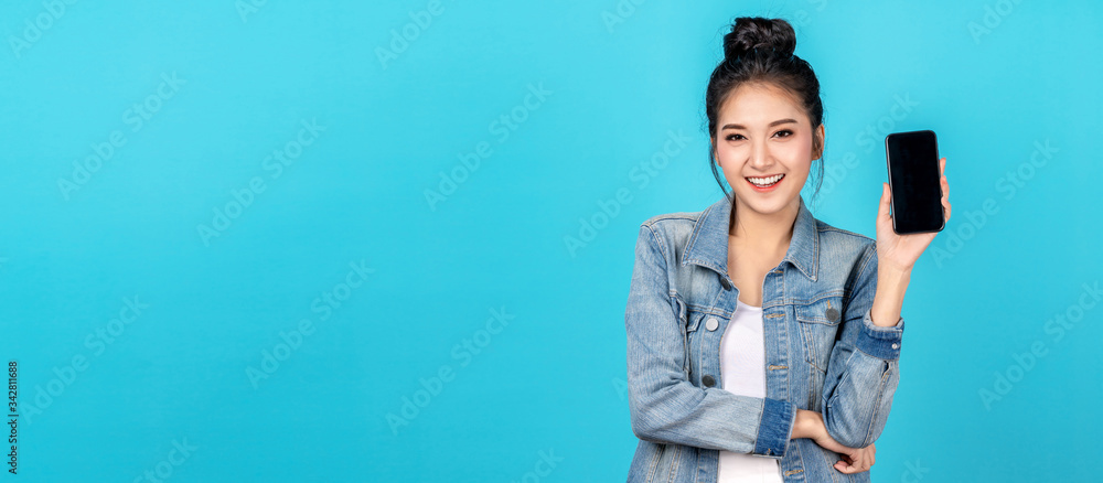 Banner of Happy asian woman feeling happiness and standing hold smartphone on blue background. Cute asia girl smiling wearing casual jeans shirt and connect internet shopping online and present Banner of Happy asian woman feeling happiness and standing hold smartphone on blue background. Cute asia girl smiling wearing casual jeans shirt and connect internet shopping online and present
