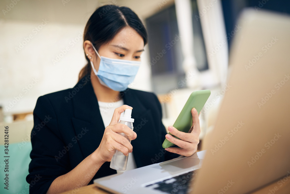 A young Asian woman cleaning and sterilizing her smartphone with alcohol spray at home office. A young Asian woman cleaning and sterilizing her smartphone with alcohol spray at home office.