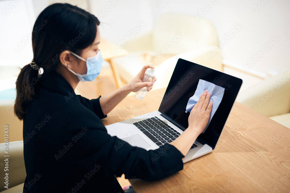 Portarit of a young Asian woman cleaning and wiping the surface of laptop with cleaning spray and antistatic cloth at home