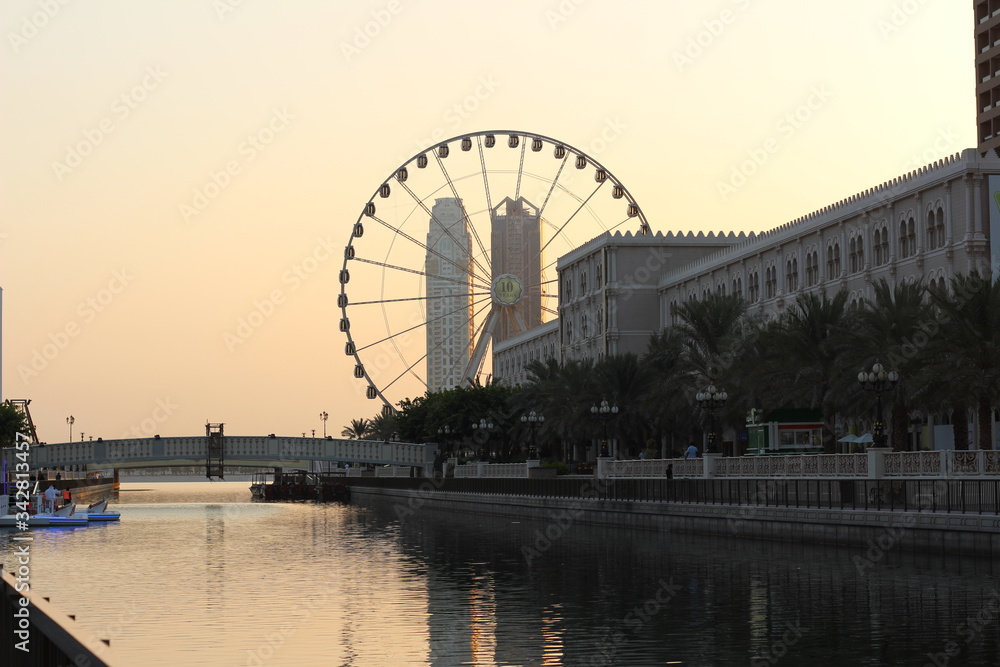 Sharjah Eye a beautiful piece of engineering visible from Qanat Al Qasba. The sun setting on this gorgeous tourist spot with tour boats prepping for night time tourists.