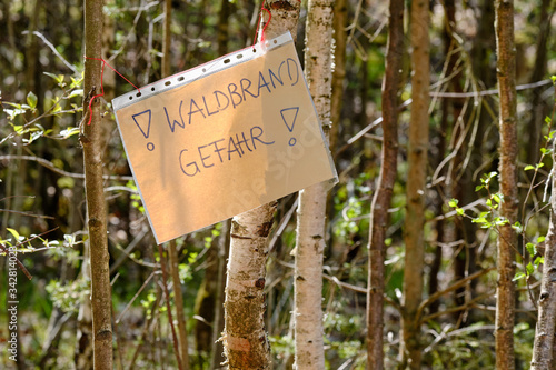A handwritten sheet of paper in a document wallet hanging between tree trunks and informing about the danger auf Waldbrandgefahr ( english wildfire risk ). Seen in Germany in Bavaria in April. © franconiaphoto