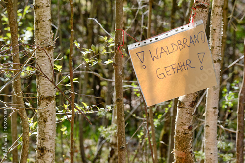 A handwritten sheet of paper in a document wallet hanging between tree trunks and informing about the danger auf Waldbrandgefahr ( english wildfire risk ). Seen in Germany in Bavaria in April.