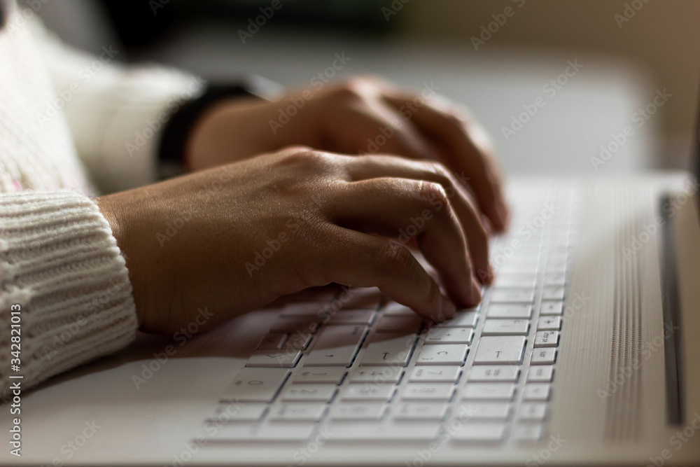 Close-up of the hands of a woman working from home with a white laptop and a smartwach in hand, with blurred background. Close-up of the hands of a woman working from home with a white laptop and a smartwach in hand, with blurred background.