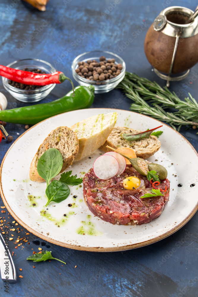 Steak Tartare with bread toasts and egg on top on blue background