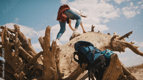 Young adventurer, woman tourist climbing on the tree trunk in the desert. Focus on the backpack in foreground.