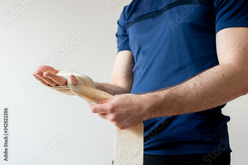 Man bandaging his hand before box training. Sporty man bandaging hands. Man injured hand and bandage it wearing blue t-shirt.