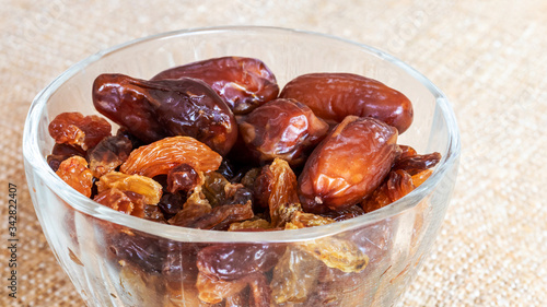 Raisins and dates in a transparent plate on a burlap background