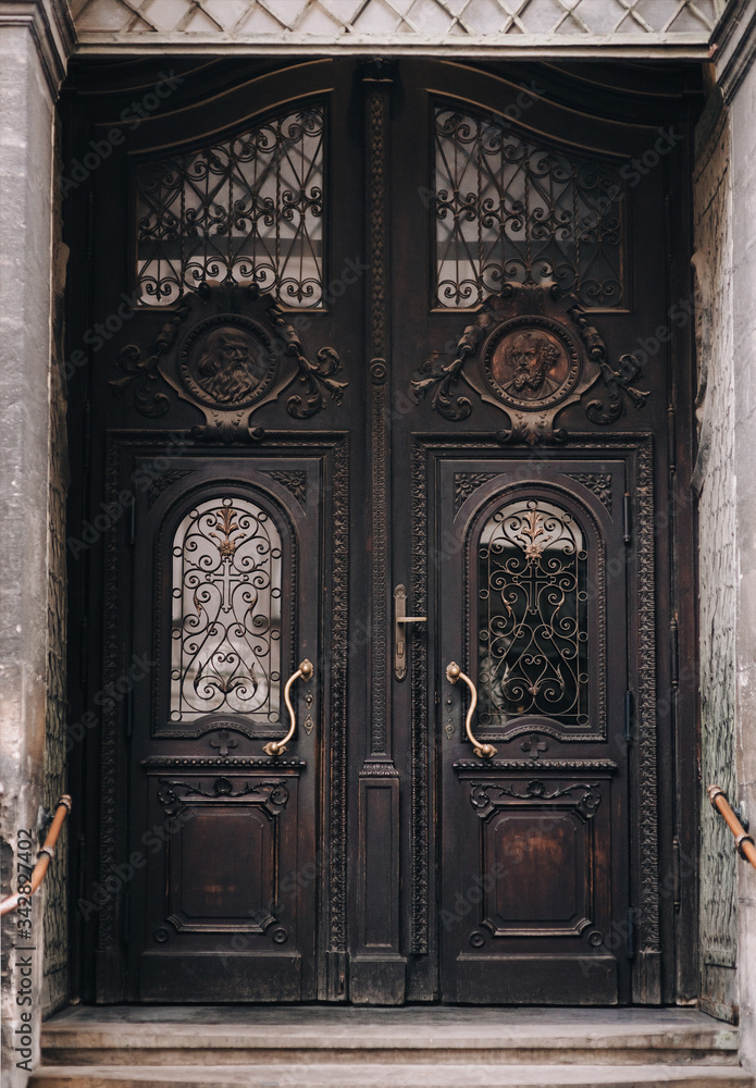 An old dark brown wooden door of the Jesuit Church in Lviv. Beautiful carvings in mahogany. Entrance to the temple. Apostle Paul and Apostle Peter. An old dark brown wooden door of the Jesuit Church in Lviv. Beautiful carvings in mahogany. Entrance to the temple. Apostle Paul and Apostle Peter.