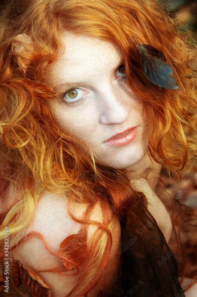Portrait of a cute young lovely redhead girl with autumnal leaves. Beautiful face of a young sexy woman among red golden foliage.
