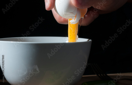Obraz na płótnie Making scrambled eggs in a white bowl in a dark background, showing the yolk int