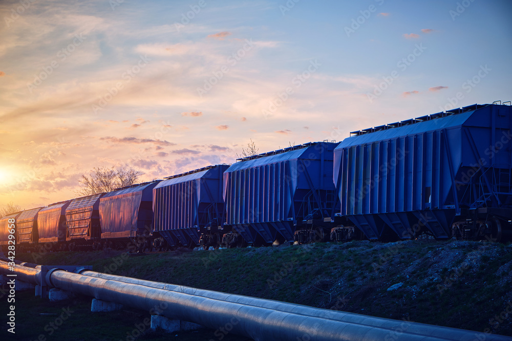 Fototapeta premium Train with wagons loaded with grain moves at sunset along the pipeline.