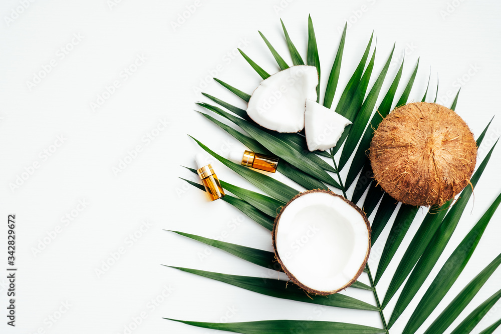 Natural coconut oil for hair, SPA organic cosmetic concept. Flat lay, top view tropical palm leaf, coconuts, essential oil bottles on white background.