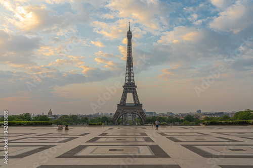 Paris, France - 04 25 2020: View of the Eiffel Tower from the Trocadero esplanade with a seatead couple and a a walking man during the coronavirus period