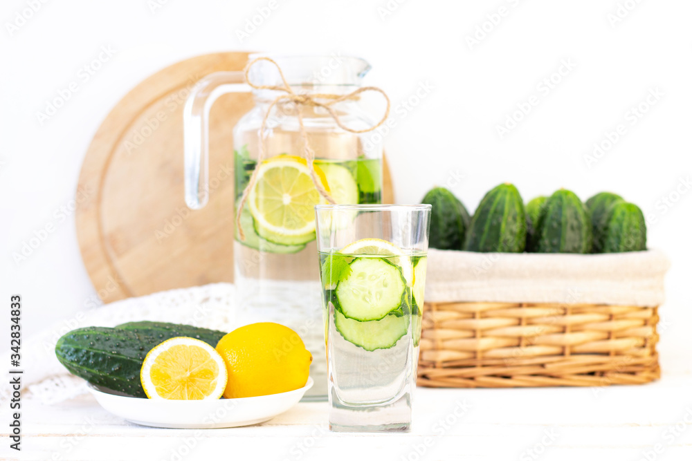 Fototapeta premium Health care, fitness, healthy eating concept. Fresh cool lemon cucumber drink with water, cocktail, detox drink, lemonade in a glass jug and a glass. cucumbers and lemon on a plate