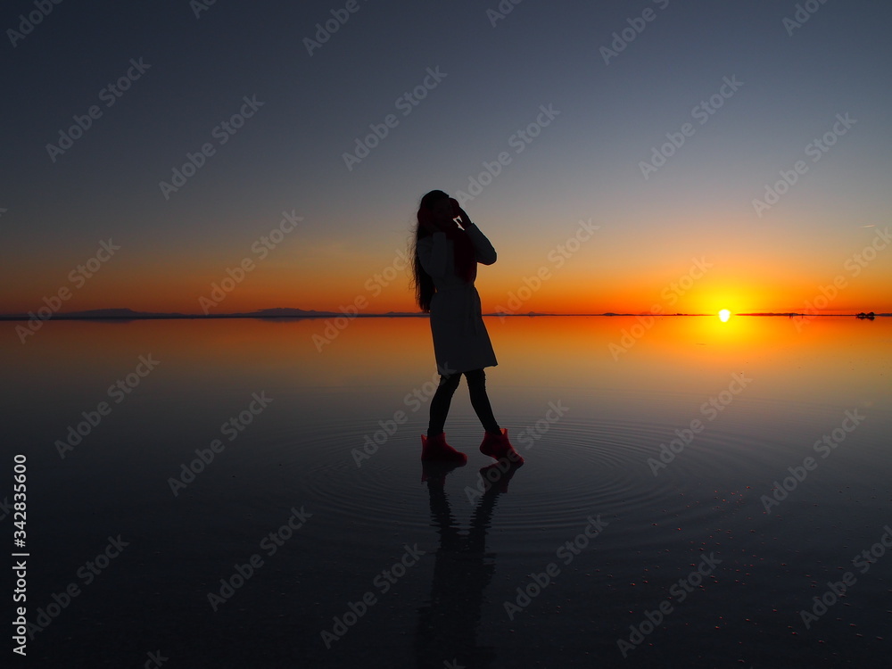 Girl model with long black hair in the white coat, red scarf and red headphones on the sunrise, Uyuni Salt Flat, Salar de Uyuni, Bolivia. Copy space for text