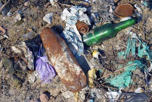 a pile of garbage from a green glass bottle with rusty cans and pieces of colored cloth in a landfill