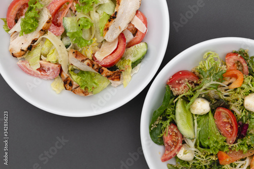 white deep plates with fresh salad ingredients mixed with sauce placed on an gray background. A place for a menu, banner or advertisement