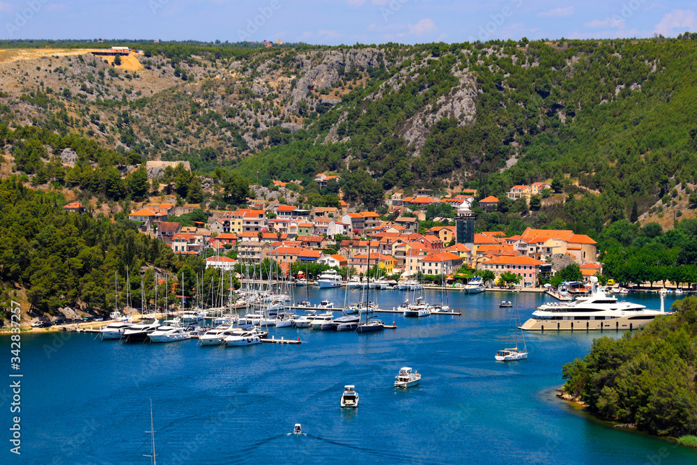 Summer landscape of the Croatian small town Skradin on Krka River. Beautiful yachts and orange buildings in the deep canyon of river. Water resources, ecology, Croatia