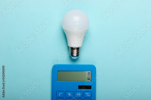 Energy saving. Calculator with led light bulb on a blue pastel background. Top view