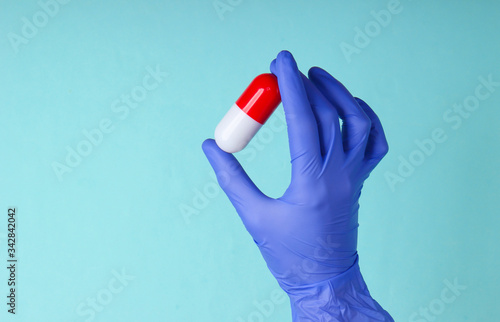 Medic's hand in latex gloves holds capsule on blue background. Medical concept