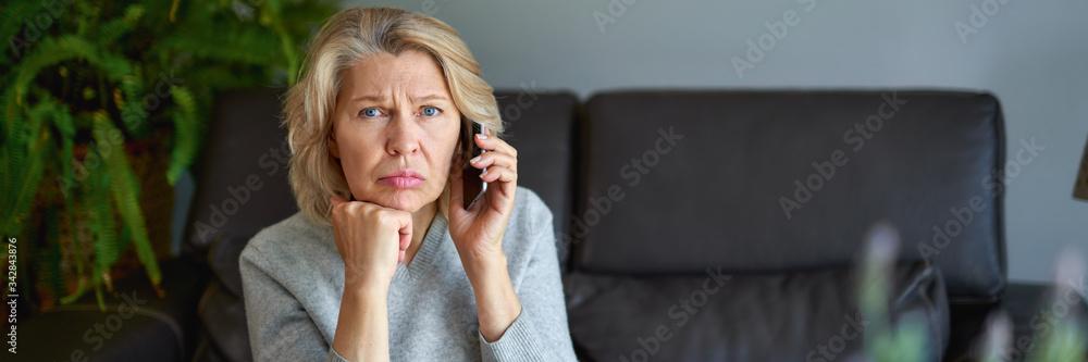 Beautiful mature blond woman talking on mobile phone at sofa