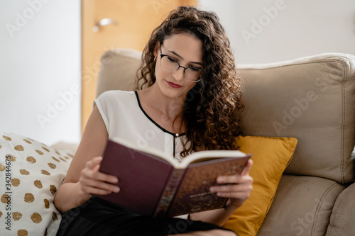 Quadro su tela Mujer joven blanca leyendo un libro con interés desde casa