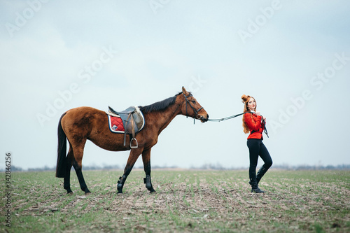 red-haired jockey girl in a red cardigan and black high boots with a horse