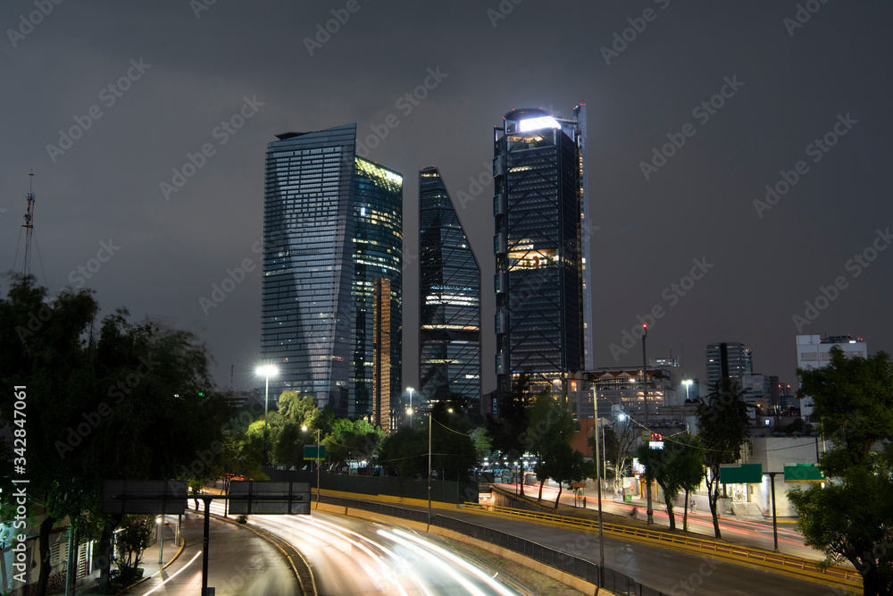 Edificios de la ciudad de México en un día lluvioso y  una avenida en la parte inferior con un barrido de luces de carros