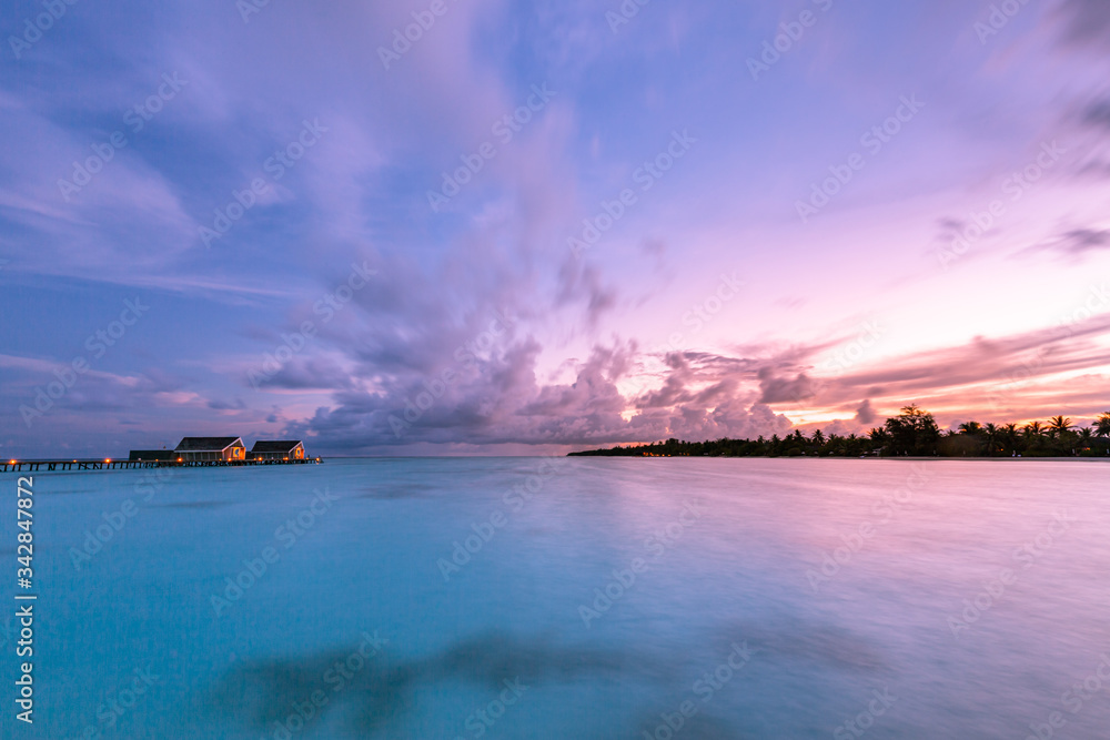Amazing sunset sky and reflection on calm sea, Maldives beach landscape of luxury over water bungalows. Exotic scenery of summer vacation and holiday background
