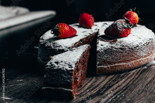 Piece of chocolate cake with strawberries on wooden table black background dark food photo