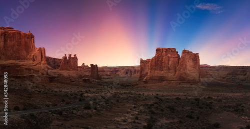 Panoramic landscape view of a Scenic road in the red rock canyons. Dramatic Colorful Sunset Sky Composite. Taken in Arches National Park, located near Moab, Utah, United States.