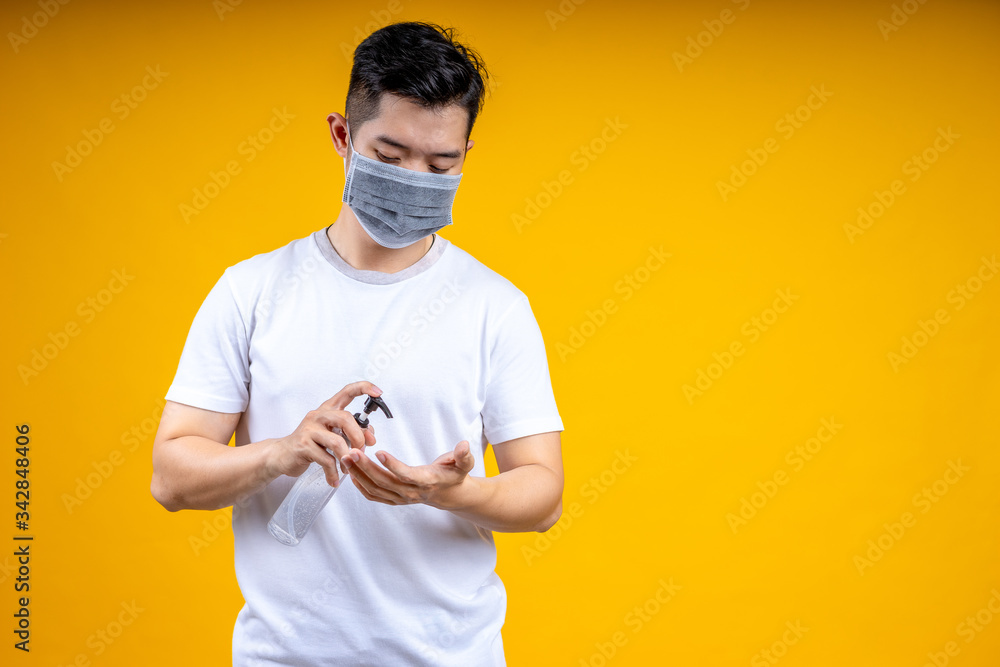 Asian man is wearing a white t-shirt and wearing a mask, holding an alcohol spray bottle. He was spraying it for cleaning or washing his hands to prevent an outbreak of coronavirus or covid-19. Asian man is wearing a white t-shirt and wearing a mask, holding an alcohol spray bottle. He was spraying it for cleaning or washing his hands to prevent an outbreak of coronavirus or covid-19.