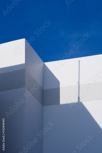 Abstract sunlight and shadow of antenna pattern on top of external white building wall surface against blue sky in vertical frame for architecture background design concept 