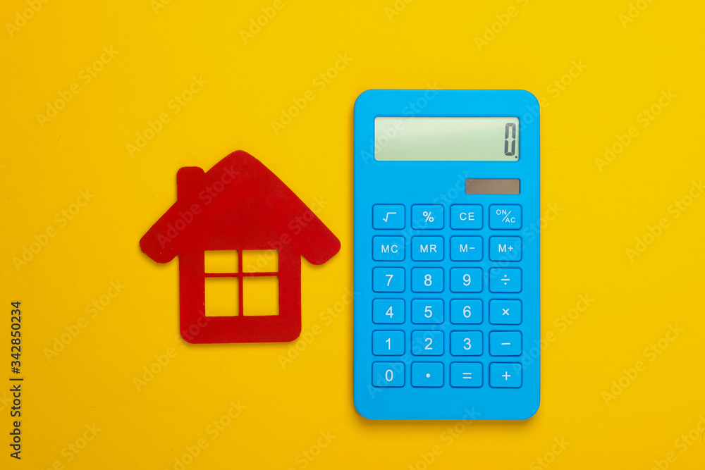 Calculation of the cost of rental housing. Red house figurine, calculator on yellow background. Top view Calculation of the cost of rental housing. Red house figurine, calculator on yellow background. Top view